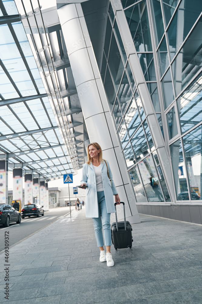 Joyous stylish passenger with baggage looking away Joyous stylish passenger with baggage looking away