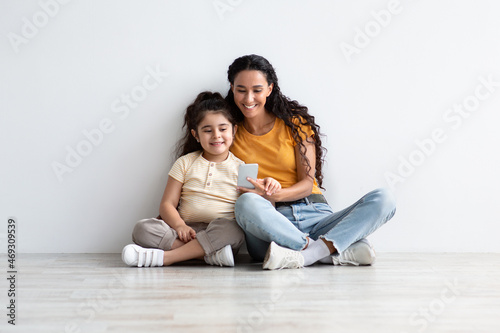 Happy Middle Eastern Mom And Little Daughter Relaxing With Smartphone At Home © Prostock-studio