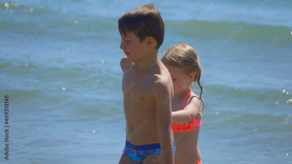 Cheerful boy and girl in pink swimsuits are running from the splashing sea waves Cheerful boy and girl in pink swimsuits are running from the splashing sea waves