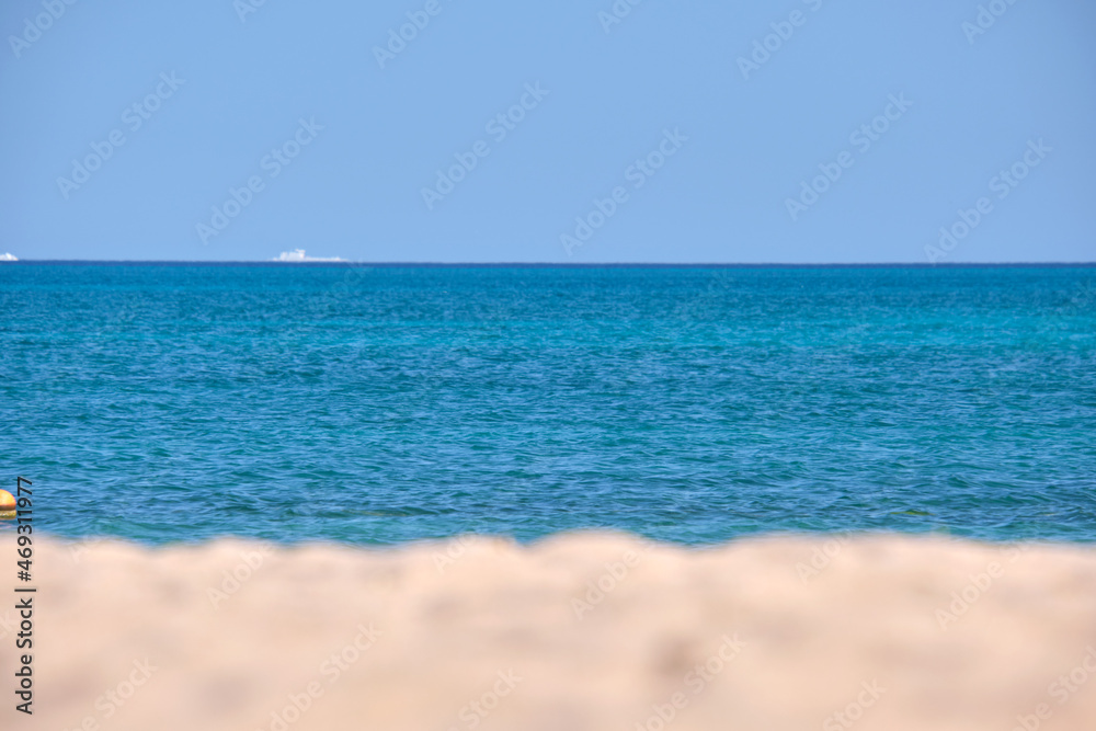 Seascape with surface of blue sea water with small ripple waves crashing on yellow sandy beach. Travel and vacations concept
