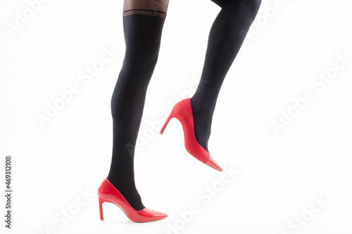 Feet of a girl in pantyhose with red shoes on a white background