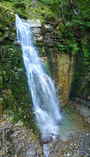 Waterfall on mountain river with white foamy water falling down from rocky formation in summer forest