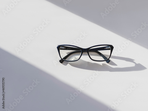 Top view of eyeglasses on white background. Comfortable life with poor eyesight. Ophthalmology. Contrast of hard sunlight and geometrical shadow. photo