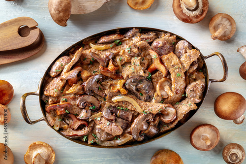Beef stroganoff, mushroom and meat ragout with cream sauce, in a cooking pan with ingredients, overhead flat lay shot on a rustic wooden background