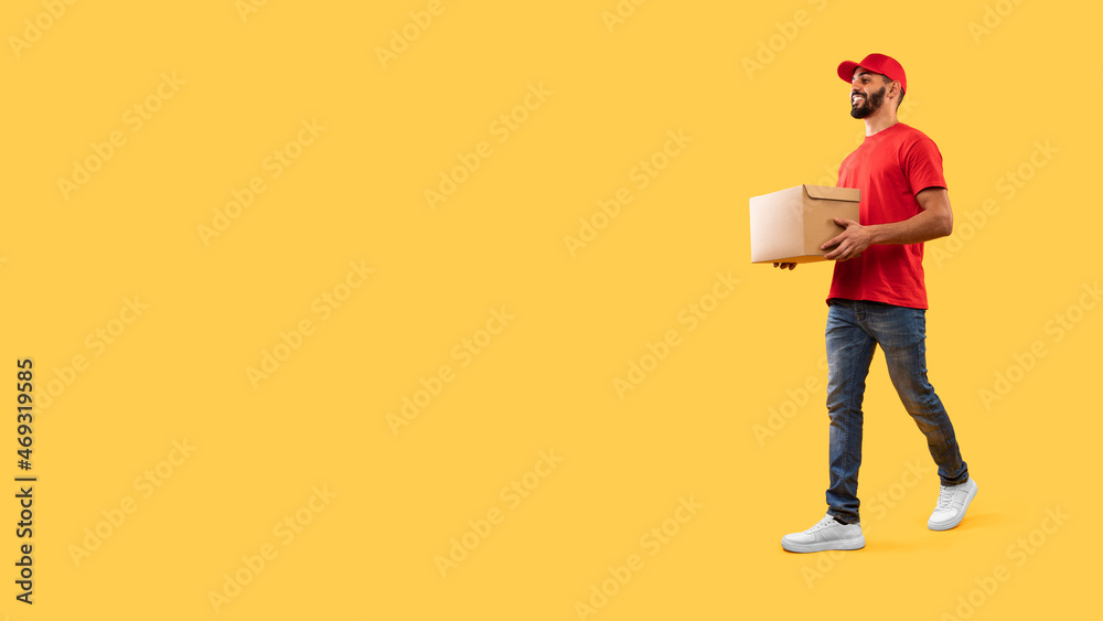 Fototapeta premium Arabic Male Courier Carrying Parcel Box Walking Over Yellow Background