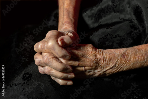 gefaltete Hände von alter Frau auf schwarzem Tuch.