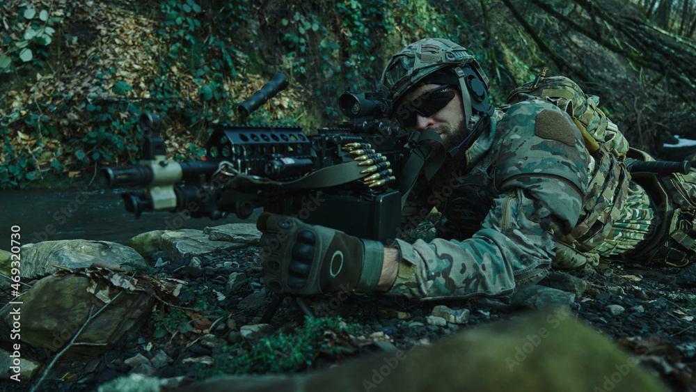Portrait of airsoft player in professional equipment in helmet aiming at victim with gun in the forest. Soldier with weapons at war Portrait of airsoft player in professional equipment in helmet aiming at victim with gun in the forest. Soldier with weapons at war