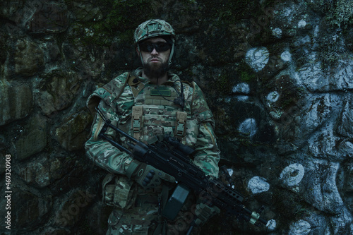 Portrait of airsoft player in professional equipment with machine gun in the forest. Soldier with weapons at war