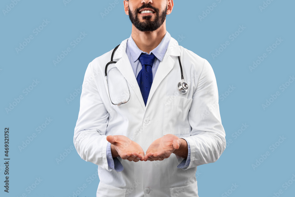 Unrecognizable Arabic Male Doctor Showing Invisible Object Over Blue Background Unrecognizable Arabic Male Doctor Showing Invisible Object Over Blue Background