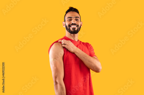 Happy Vaccinated Arabic Male Showing Arm After Vaccination, Yellow Background
