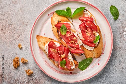 Open sandwiches with strawberries, soft cheese mint and walnut in ceramic plate on a light grey stone background. Summer and healthy dieting food, vegetarian food concept. Top view.