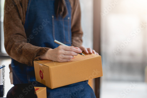Online sales business owner woman is taking note of the customer's address on the parcel box being prepared for delivery.