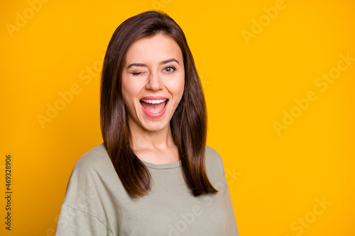 Portrait of lovely funny cheerful brown-haired girl winking having fun isolated over bright yellow color background