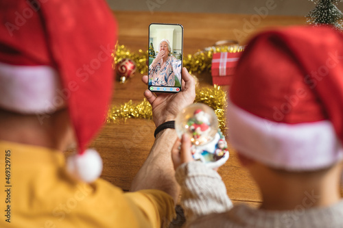 Father and son in santa hats making smartphone christmas video call with happy senior woman