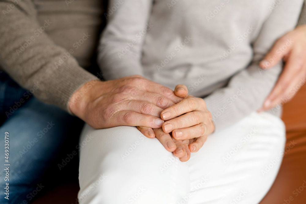 Close-up picture of hands of middle-aged couple holding hands sitting together at home, faces is not visible. Concept of support and caring in marriage Close-up picture of hands of middle-aged couple holding hands sitting together at home, faces is not visible. Concept of support and caring in marriage