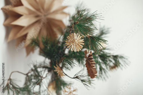 Stylish christmas straw ornaments and paper angel on pine branches against sweden star. Eco decor