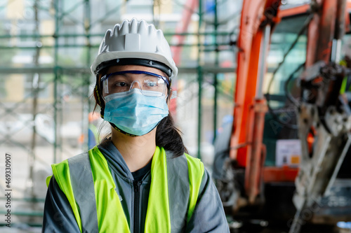 Portrait of an Asian female engineer Put on a brightly colored shirt. and wear a white safety cap standing with his arms crossed at the construction site