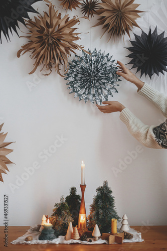 Hands arranging paper sweden stars on wall and christmas candles, pine trees decor on rustic table