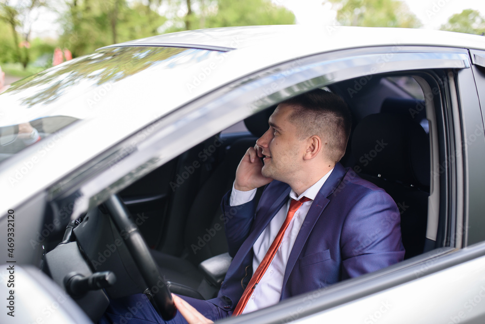 A male business man is talking on the phone in a car.