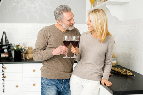Slika na platnu Romantic middle-aged couple holding glasses of wine look at each other and smile