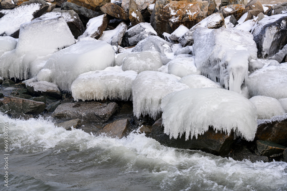 A wave runs over coastal rocks in the cold, covering them with ice and icicles A wave runs over coastal rocks in the cold, covering them with ice and icicles