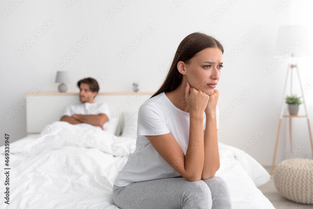 Upset unhappy offended angry millennial european wife sitting on bed, ignoring husband with crossed arms Upset unhappy offended angry millennial european wife sitting on bed, ignoring husband with crossed arms