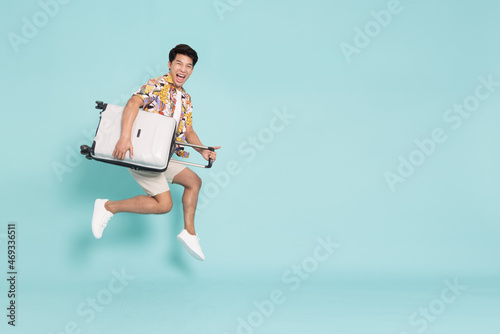 Happy Young Asian traveler man jumping with suitcase bag isolated on green background, Tourist in summer and holidays vacation concept photo