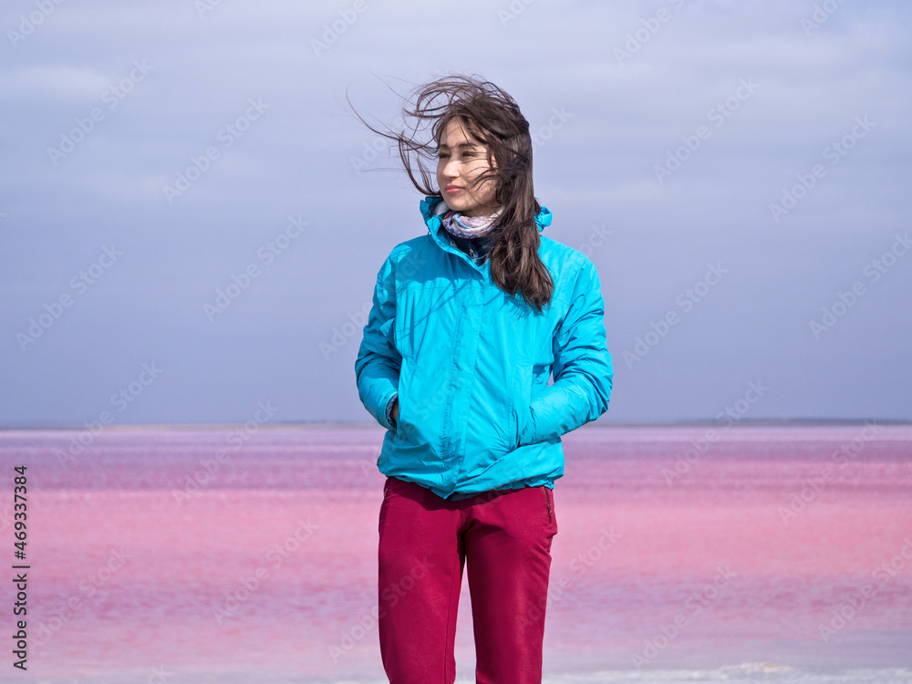 Woman at pink salt lake water background at windy sunny day