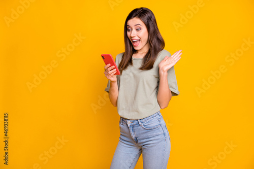 Photo of astonished happy young woman hold phone read notification sale isolated on vivid yellow color background
