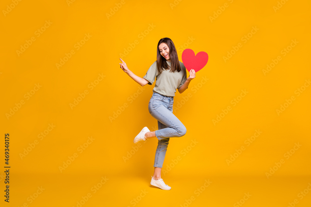 Full size photo of attractive nice woman point finger empty space dream hold red paper heart isolated on yellow color background