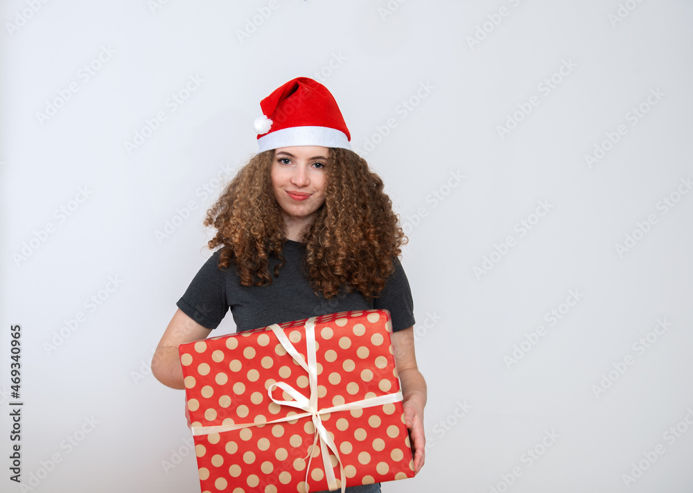 Happy excited young woman in santa claus hat with curly hair and gift box over white background