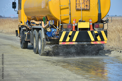 A yellow sprinkler truck sprinkling water on unpaved roads. photo