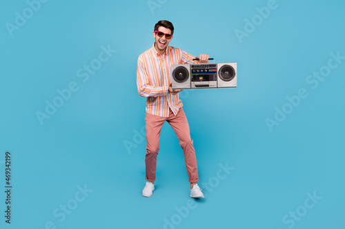 Full body photo of positive joyful happy man hold hands boombox wear sunglass isolated on blue color background