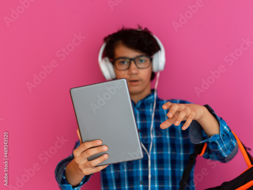 portrait of an arab teenager with headphones, a backpack and a tablet isolated on a purple background while watching online classes during the corona virus pandemic