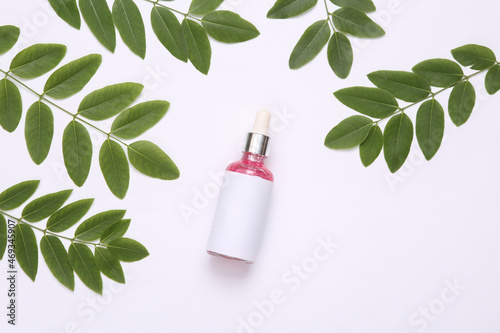 Bottle of face serum with sprigs of green leaves on white background. Natural cosmetics concept