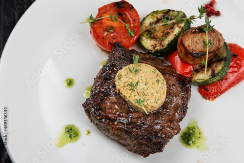 Grilled black angus strip loin steak with vegetables on white plate on black wooden background