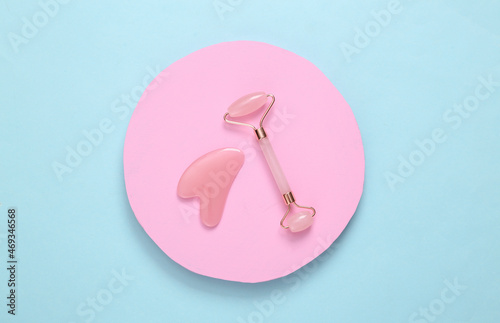 Face roller and gua sha stone massager on pink circle. Blue background. Top view photo