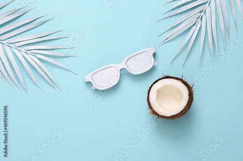 White sunglasses, coconut and palm leaves on blue background. Minimal travel, tropical layout. Top view