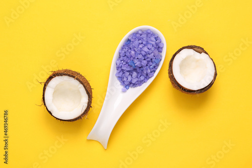Spoon with sea bath salt and coconut on yellow background. Top view