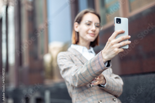 Stylish young business woman taking a selfie on a smartphone against the background of a business building