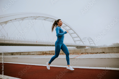 Young woman in blue track suit running by the river at autumn morning © BGStock72