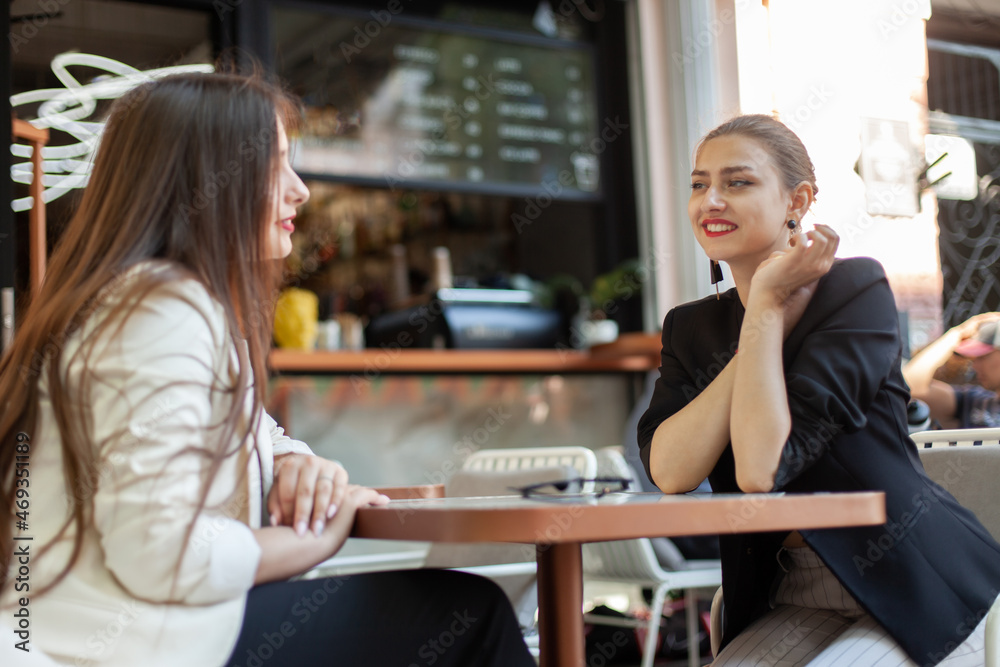 Two cute women friend talking while discussing while sitting at table in outdoor cafe