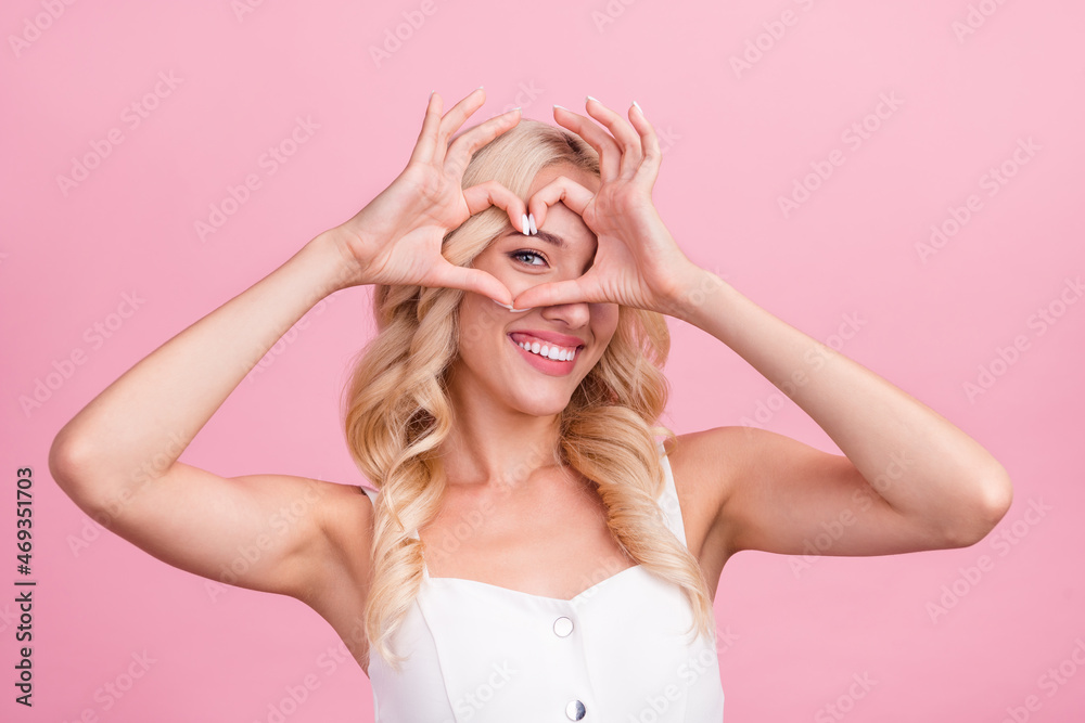 Photo of young attractive girl happy positive smile show fingers heart figure look eye romantic isolated over pink color background Photo of young attractive girl happy positive smile show fingers heart figure look eye romantic isolated over pink color background