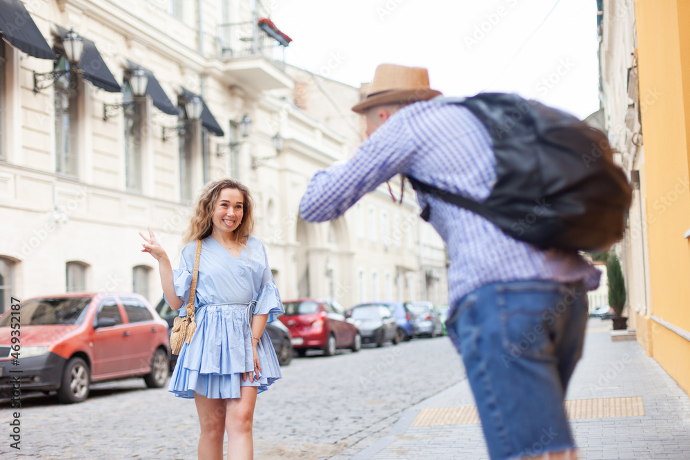 A man photographs a young pretty woman on a European street. Young couple of tourists. Travel concept