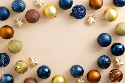 Frame made of colorful Christmas baubles on pastel beige background. Bronze, golden and blue Christmas balls. Flat lay, top view, copy space.