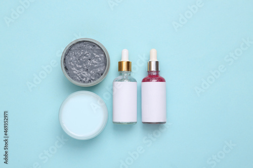 Bottles of face serum and jar of black clay, cream on blue background. Top view