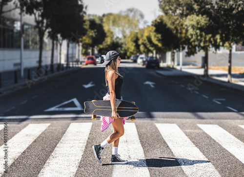 a young girl crosses a crosswalk with a skateboard in her hand. cityscape concept.