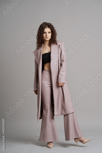 Studio shot of pretty fashion model in pastel purple leather trousers and coat on gray background