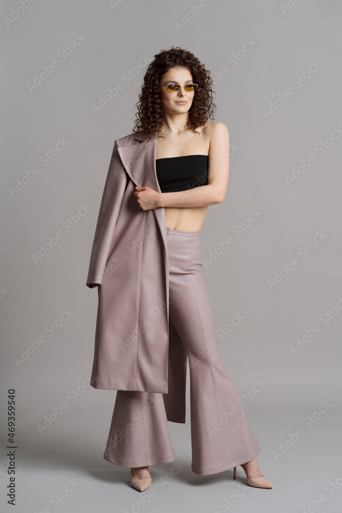 Studio shot of pretty fashion model in pastel purple leather trousers, coat, khaki sunglasses on gray background Studio shot of pretty fashion model in pastel purple leather trousers, coat, khaki sunglasses on gray background