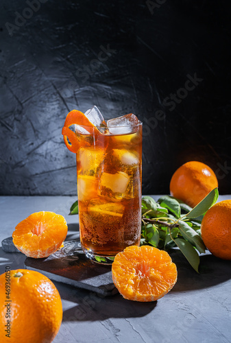 Chinotto drink in the glass with ice and fruits on the grey table photo